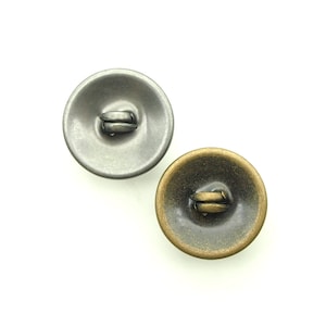 May include: Two round metal buttons with a shank. One button is silver and the other is gold.