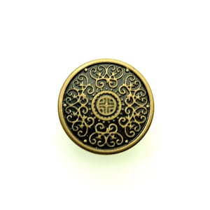 May include: A round, antique brass button with an ornate, swirling design. The button features a central emblem and a dark, contrasting background, creating a vintage aesthetic. Ideal for sewing and craft projects.
