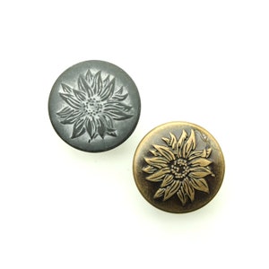 May include: Two metal buttons with a sunflower design. One button is silver with a black sunflower, and the other is gold with a brown sunflower.