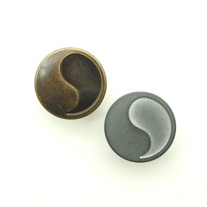 May include: Two round metal buttons with a yin yang symbol design. One button is gold and the other is silver.