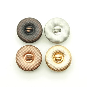 May include: Four decorative buttons in different colors: copper, gold, silver, and bronze. Each button has a raised, textured design and a shank for sewing.