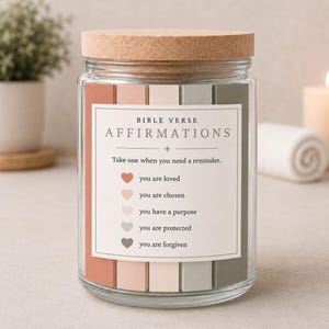 May include: A glass jar with a cork lid filled with affirmation cards. The label says "BIBLE VERSE AFFIRMATIONS" with phrases such as "you are loved" and "you are forgiven." The jar has a neutral colour scheme with pink, beige, and green accents.