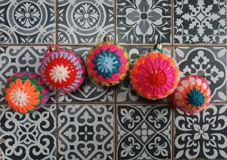 K&ouml;nnte beinhalten: Sechs bunte geh&auml;kelte Weihnachtskugeln mit verschiedenen Mustern und Farben, darunter Rosa, Rot, Orange, Gelb, Gr&uuml;n, Blau und Wei&szlig;.