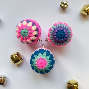 K&ouml;nnte beinhalten: Drei geh&auml;kelte Weihnachtskugeln in Rosa, Blau, Gr&uuml;n und Wei&szlig;. Die Kugeln sind rund und haben ein Sternmuster.