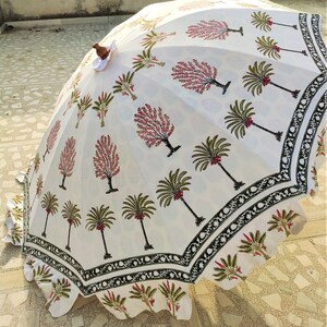 May include: A white cotton umbrella with a black and green border. The umbrella is decorated with a floral pattern of pink flowers and green palm trees.