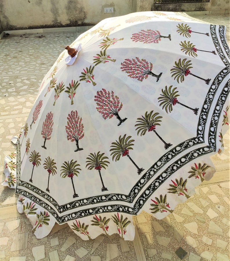 May include: A white cotton umbrella with a black and green border. The umbrella is decorated with a floral pattern of pink flowers and green palm trees.