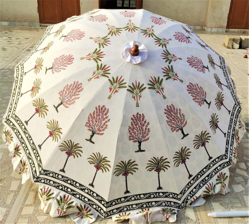 May include: A white cotton patio umbrella with a black and green border. The umbrella features a repeating pattern of pink and green trees.