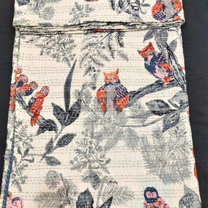 May include: A white kantha quilt with a repeating pattern of owls and branches. The owls are in shades of blue, pink, and orange. The branches are in shades of gray. The quilt is made of cotton and is hand-stitched.