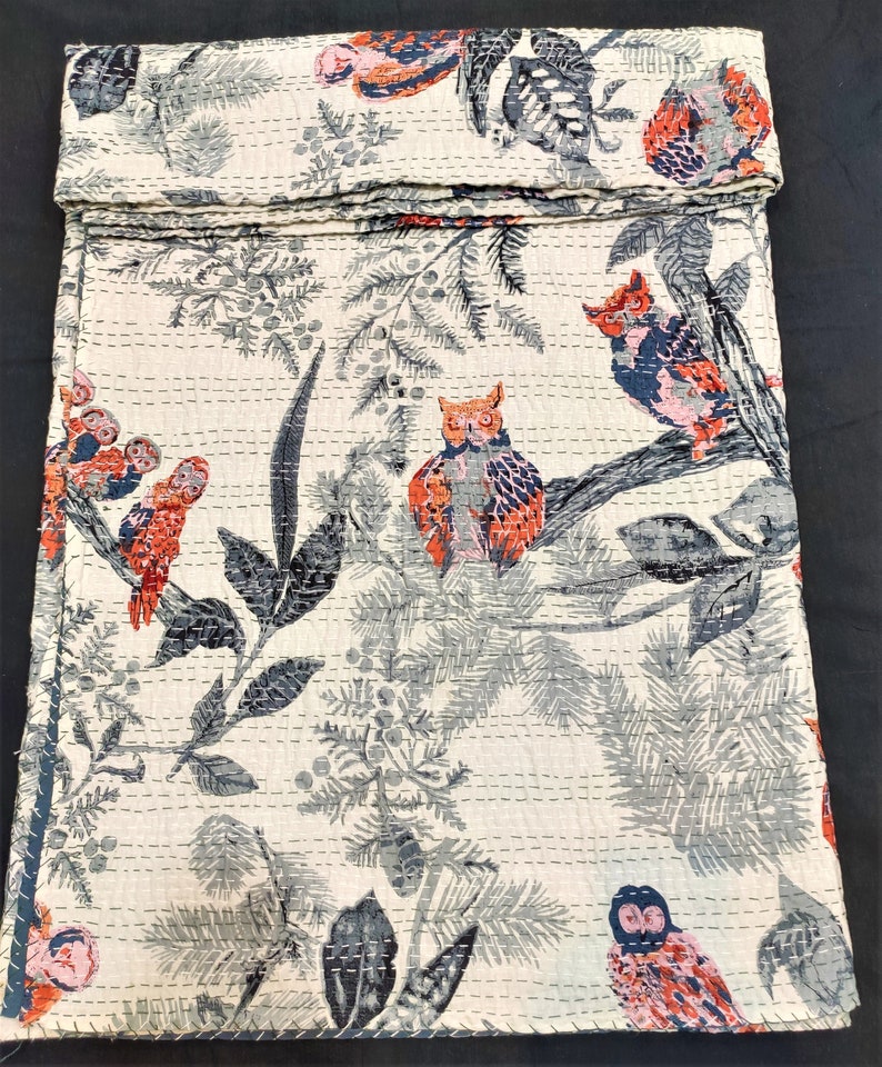 May include: A white kantha quilt with a repeating pattern of owls and branches. The owls are in shades of blue, pink, and orange. The branches are in shades of gray. The quilt is made of cotton and is hand-stitched.