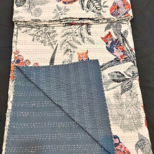 May include: A white kantha quilt with a blue backing. The quilt features a repeating pattern of owls and floral designs in shades of gray, pink, and red.