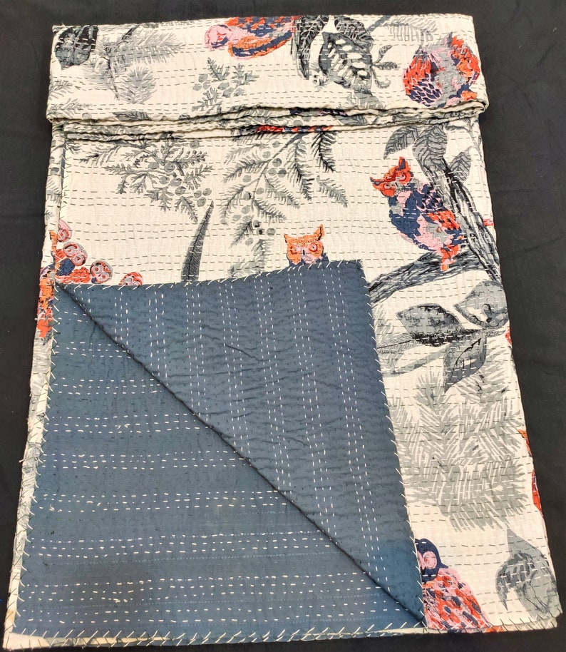 May include: A white kantha quilt with a blue backing. The quilt features a repeating pattern of owls and floral designs in shades of gray, pink, and red.
