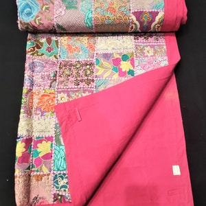 May include: A patchwork quilt featuring a variety of colourful floral and geometric fabric squares in shades of pink, blue, yellow, and green. The quilt has a solid hot pink border and a plain hot pink underside, with visible stitching between squares.