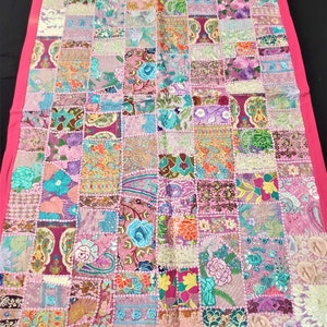 May include: A pink patchwork quilt featuring a range of floral patterns and colours. The quilt is made from various fabrics and textures, and it has a pink border.
