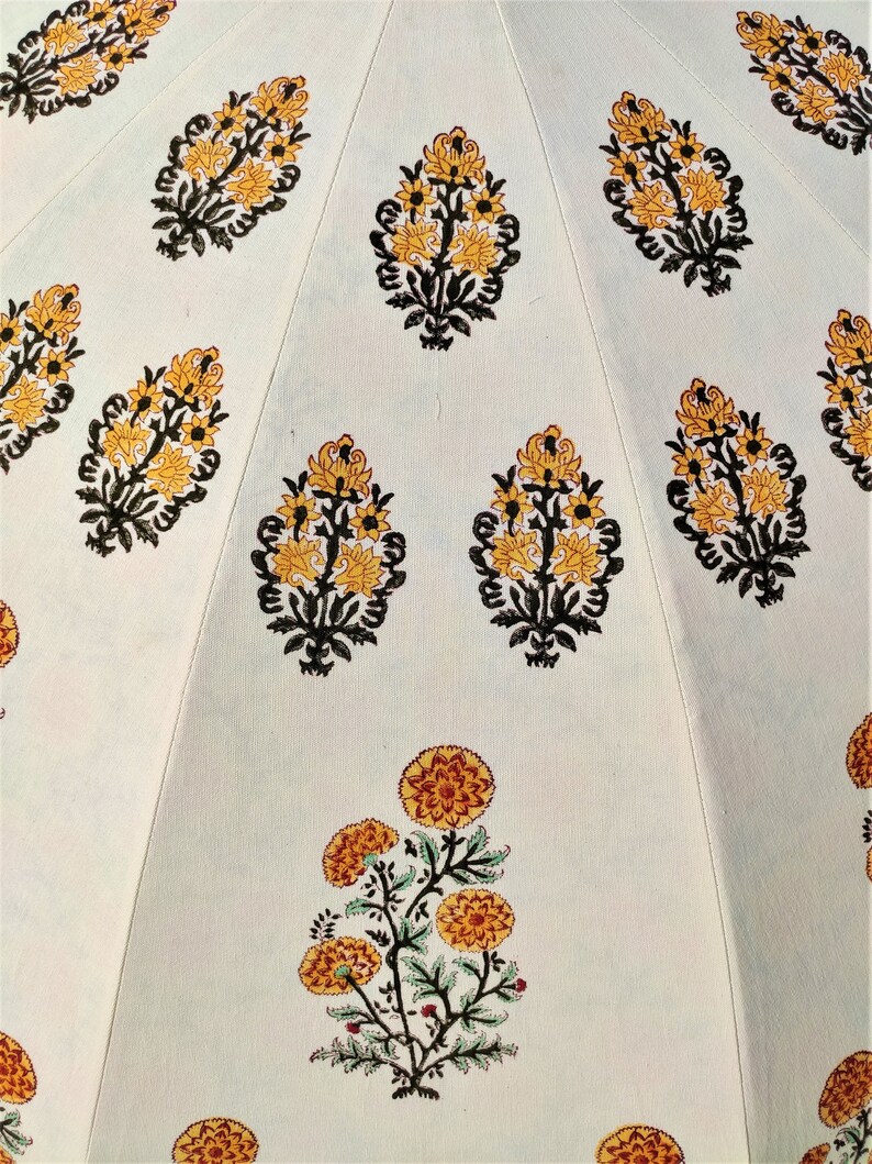 K&ouml;nnte beinhalten: Eine hellfarbige Stoffoberfl&auml;che mit einem sich wiederholenden Muster aus gedruckten Blumenmotiven. Das Design zeigt gelbe und orangefarbene Bl&uuml;ten mit schwarzen Stielen und Bl&auml;ttern, die in vertikalen Abschnitten durch feine N&auml;hte getrennt sind.