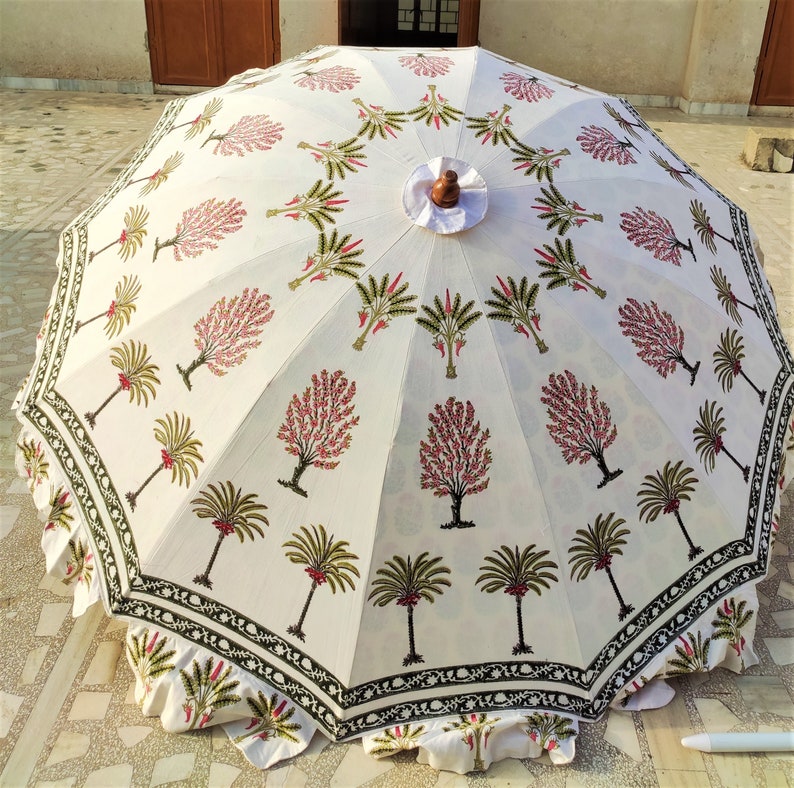 May include: A white patio umbrella with a green and pink floral print. The umbrella has a wooden handle and a white fabric canopy.