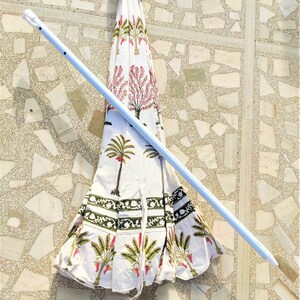 May include: A white and green patterned umbrella with a white metal pole. The umbrella is closed and lying on a tiled floor.
