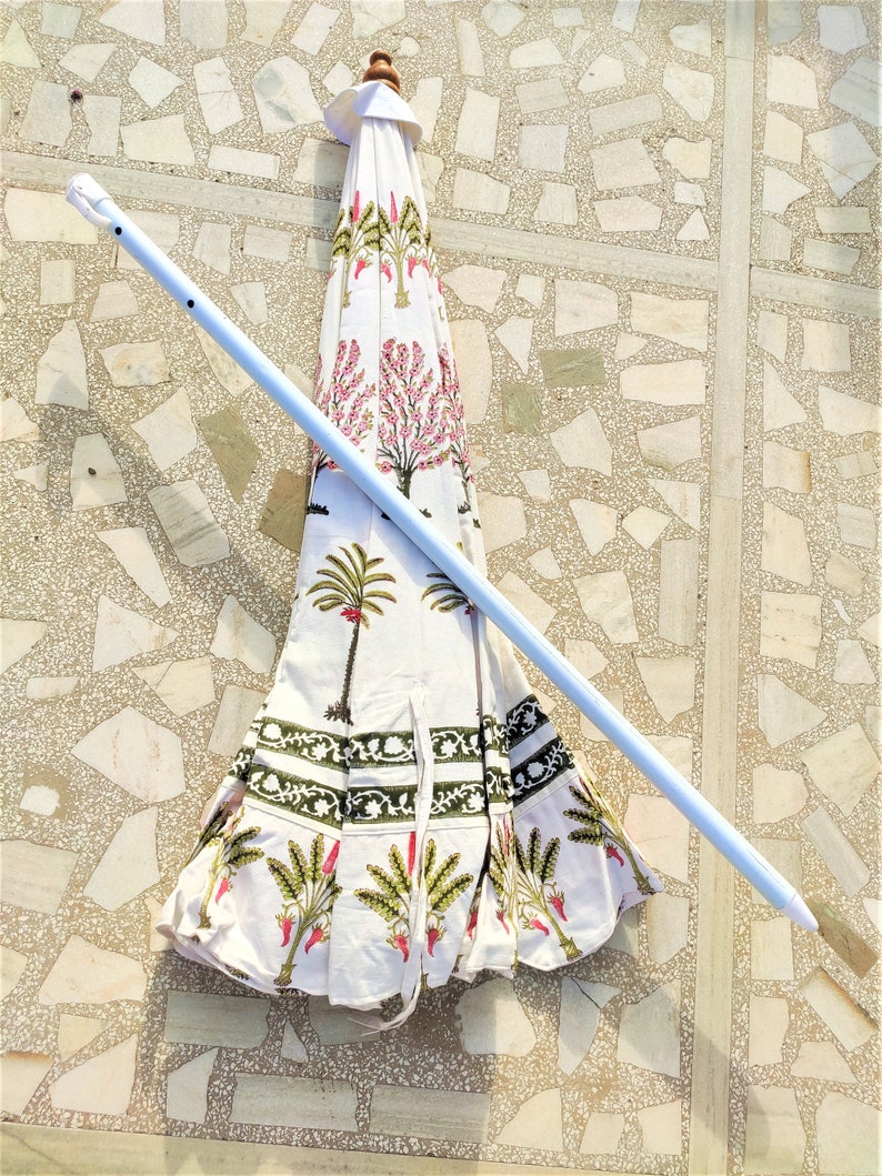 May include: A white and green patterned umbrella with a white metal pole. The umbrella is closed and lying on a tiled floor.