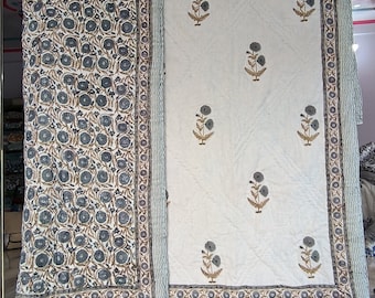 May include: Two white cotton quilts with a floral print. One quilt has a repeating pattern of small blue flowers and the other has a larger floral design with gray flowers. Both quilts have a brown and white border.