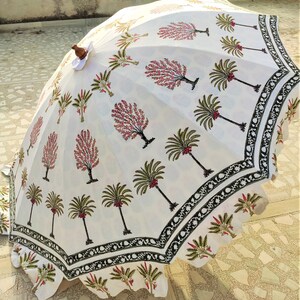 May include: White cotton umbrella with a black and green border. The umbrella is decorated with a repeating pattern of pink and green trees.