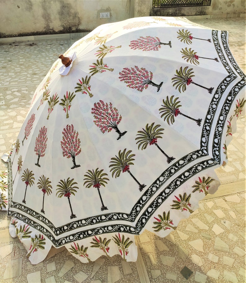 May include: White cotton umbrella with a black and green border. The umbrella is decorated with a repeating pattern of pink and green trees.