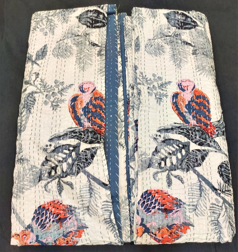 May include: A white kantha quilt with a blue border. The quilt features a repeating pattern of birds and leaves in shades of gray, blue, pink, and orange.