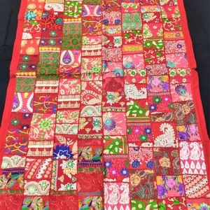 May include: A rectangular wall hanging featuring a patchwork design of various fabric squares in shades of red, pink, green, and gold. The textile displays intricate embroidery, floral patterns, paisley motifs, and sequins, finished with a red border.
