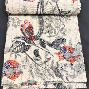 May include: A white kantha quilt with a black and gray floral pattern and red and pink birds. The quilt is folded and rolled up.