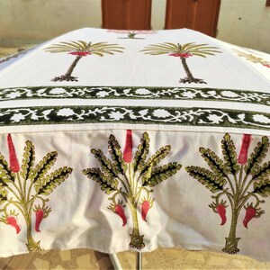 May include: White cotton umbrella with a green and red floral print. The umbrella has a double border of green and white floral designs. The umbrella is closed and sitting on a table.