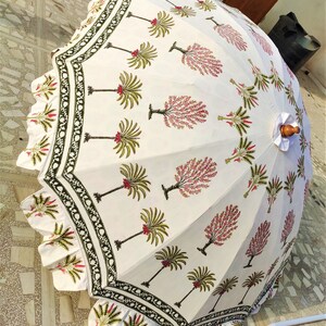 May include: A white cotton umbrella with a green and pink floral print. The umbrella has a scalloped edge and a wooden handle.