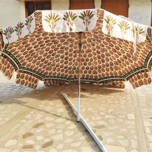 May include: A white and beige patterned umbrella with a black trim and a silver metal pole. The umbrella is closed and lying on a tiled floor.