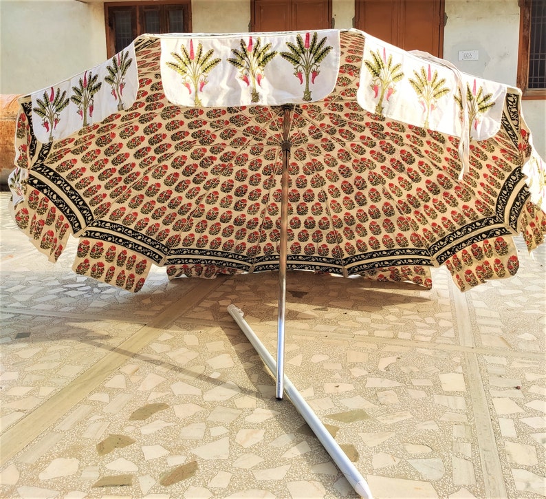 May include: A white and beige patterned umbrella with a black trim and a silver metal pole. The umbrella is closed and lying on a tiled floor.
