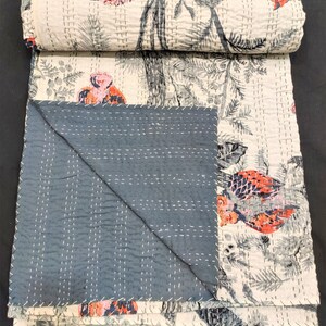 May include: A white and gray kantha quilt with a floral and bird print. The quilt is folded in half and has a dark blue backing.