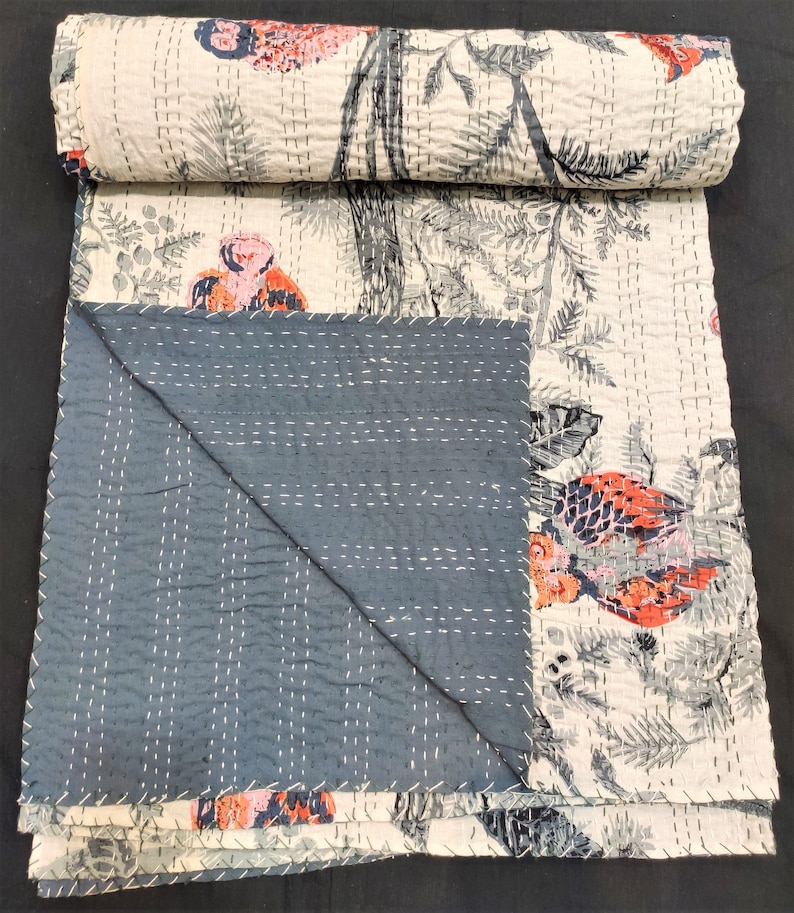 May include: A white and gray kantha quilt with a floral and bird print. The quilt is folded in half and has a dark blue backing.