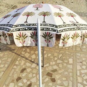 May include: White cotton patio umbrella with a green and pink floral print. The umbrella is open and the pole is white.