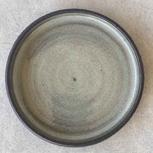 May include: A round ceramic plate with a dark gray rim and a light gray speckled surface.