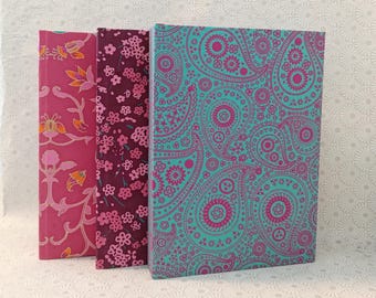 Puede incluir: Tres cuadernos con diferentes cubiertas estampadas. El primer cuaderno tiene un diseño floral rosa, el segundo cuaderno tiene un diseño floral burdeos y el tercer cuaderno tiene un diseño paisley turquesa.