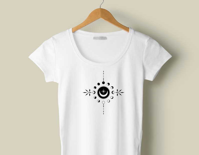 May include: White t-shirt with a black moon phases design. The design features a crescent moon with a star inside, surrounded by a circle of moon phases.