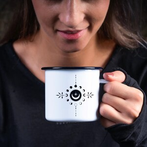 May include: A white enamel mug with a black and white moon phase design. The mug has a black rim and handle.