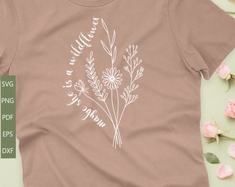May include: A light brown t-shirt with the text "She is a wildflower" written in a cursive font. The text is surrounded by a white outline of a bouquet of flowers.