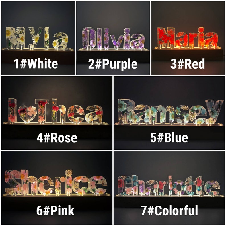 May include: Seven different names spelled out in illuminated letters with pressed flowers inside. The names are Myla, Olivia, Maria, Thea, Ramsey, Sherice, and Charlotte. Each name is displayed on a separate wooden base with a number and color label. The colors are white, purple, red, rose, blue, pink, and colorful.
