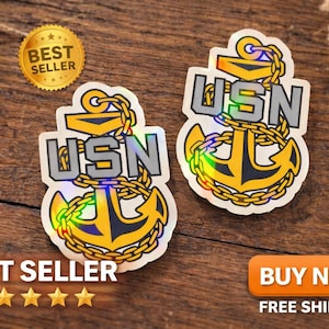 May include: Two USN anchor stickers with a gold and silver design. The stickers have a holographic effect and are on a wooden surface. The words "BEST SELLER" and "BUY NOW" are also visible.