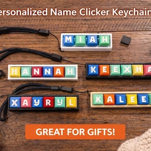 May include: Personalised name clicker keychains with colourful letter tiles spelling out names. Each keychain has a black wrist strap. The keychains are displayed on a wooden surface. The text "GREAT FOR GIFTS!" is in an orange rectangle.