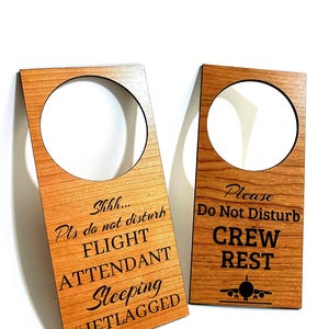 May include: Two wooden door hangers with a light brown finish. One reads "Shhh... Pls do not disturb FLIGHT ATTENDANT Sleeping #JETLAGGED." The other says "Please Do Not Disturb CREW REST" with an airplane graphic.