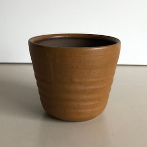 Könnte beinhalten: Ein brauner Keramiktopf mit einem strukturierten, gerippten Design.