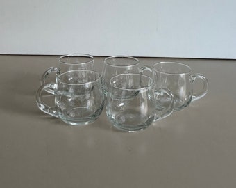 May include: Set of six clear glass mugs with handles. The mugs are round and have a slight curve to them.