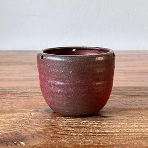 Könnte beinhalten: Ein kleiner, dunkelroter Keramiktopf mit einer strukturierten Oberfläche und Abzugslöchern. Der Topf ist perfekt für kleine Pflanzen oder Sukkulenten.