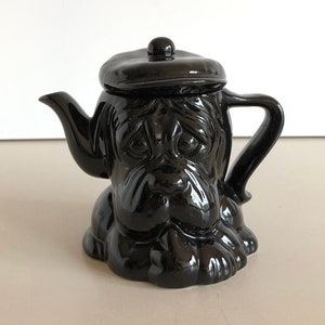 Könnte beinhalten: Schwarze Keramik-Teekanne in Form eines Hundes mit Hut. Die Teekanne hat einen Ausguss und einen Griff.