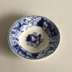 Könnte beinhalten: Eine weiße Keramikschale mit einem blauen und weißen Blumenmuster. Die Schale hat einen gewellten Rand und einen erhöhten Rand.