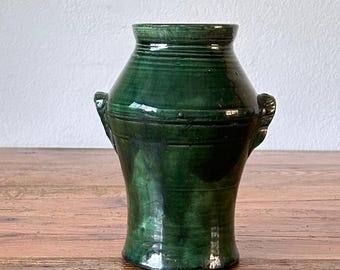 May include: A green ceramic vase with two handles. The vase has a glossy finish and is decorated with horizontal lines.