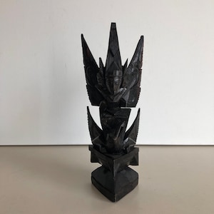 May include: A dark wood carved sculpture of a mythical creature with wings and a human face. The sculpture is in a standing position and has a pointed crown.